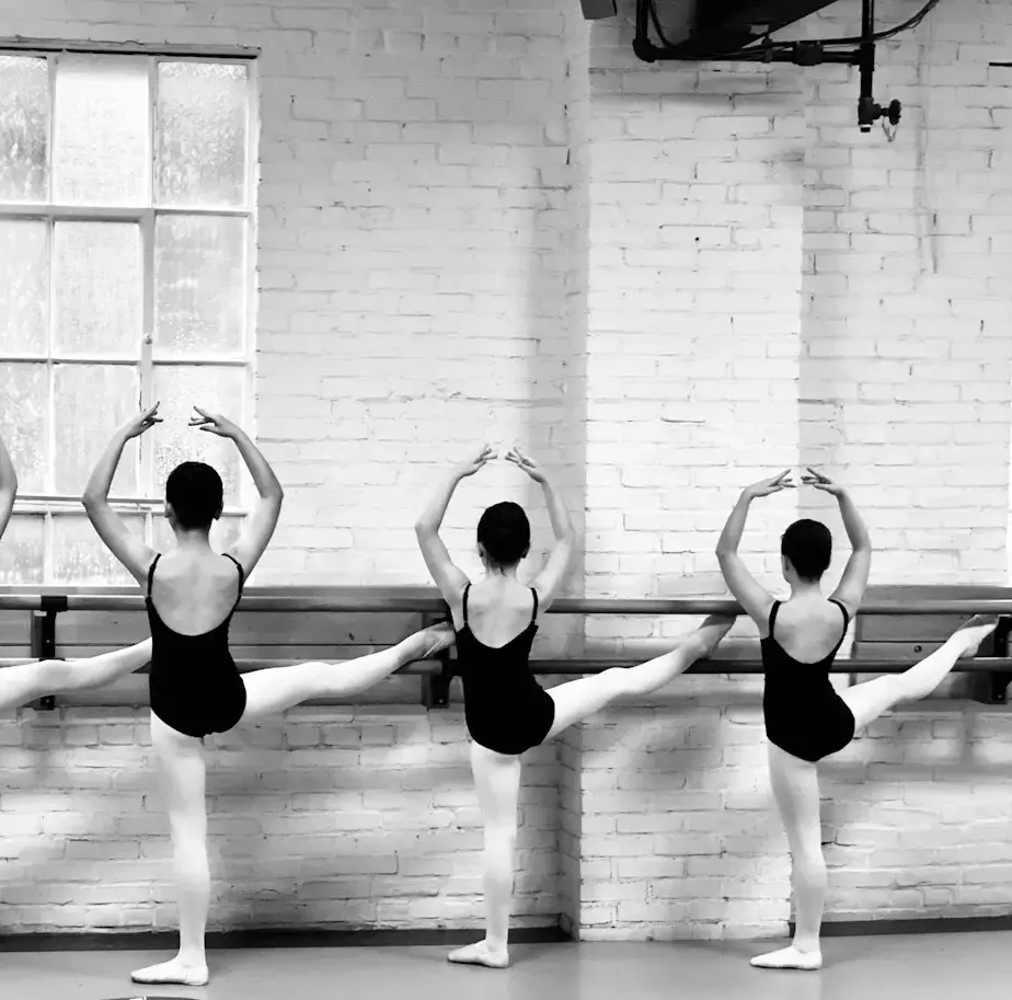A line of dancers at the barre with arms raised in fifth position