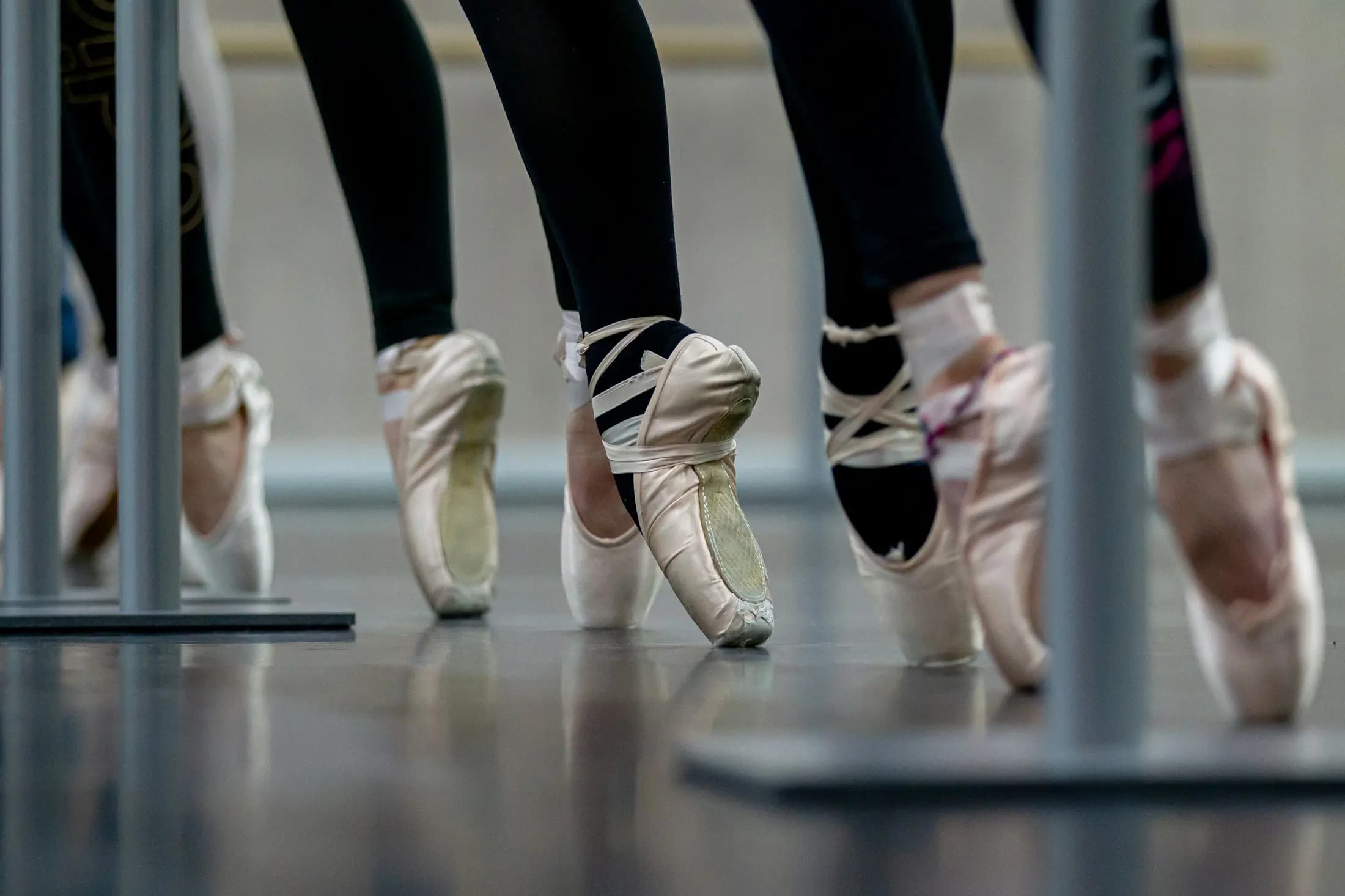 Dancers' feet in ballet shoes at a studio barre