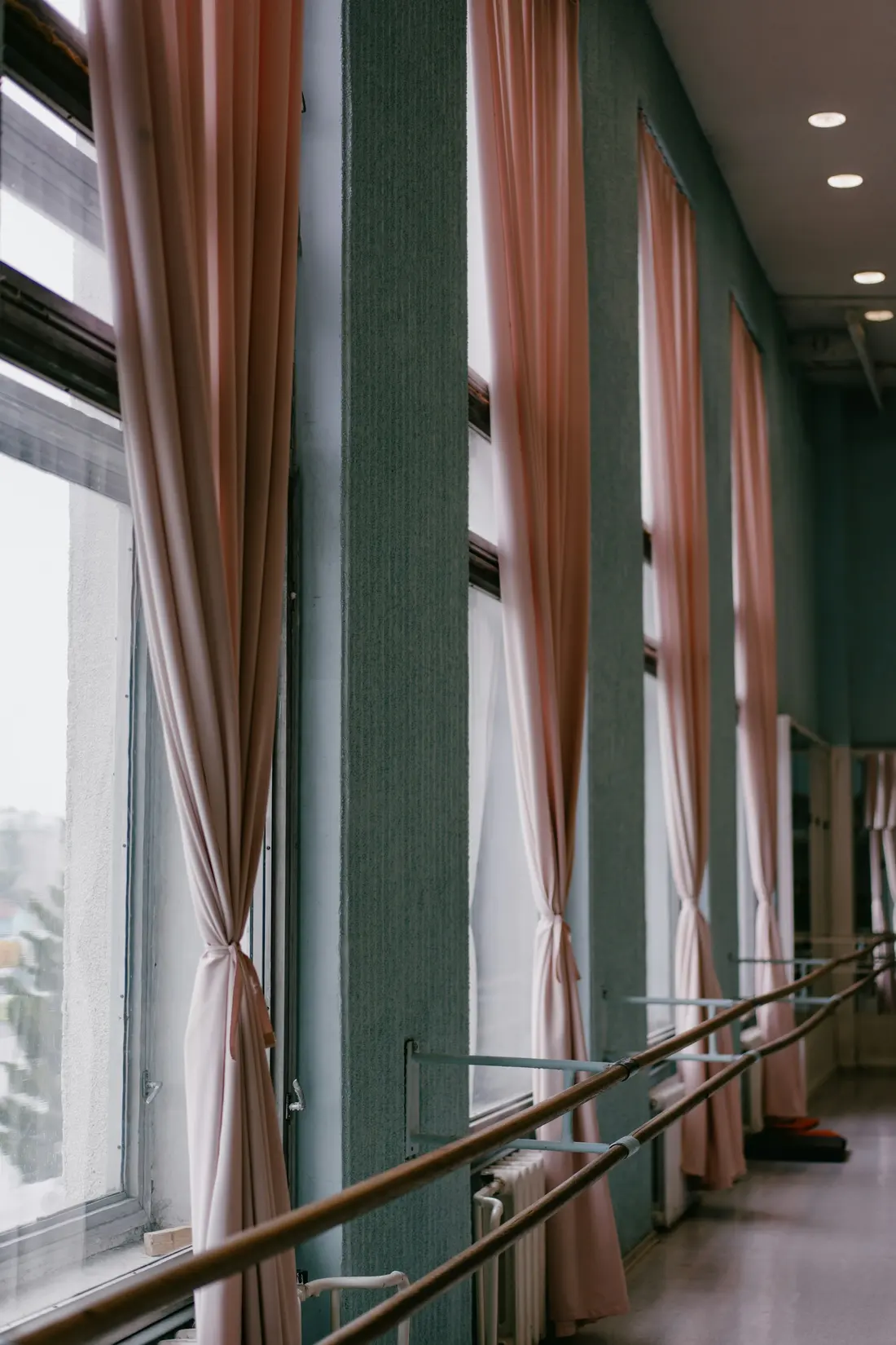 An empty ballet studio with pink curtains and a wooden barre along the windows